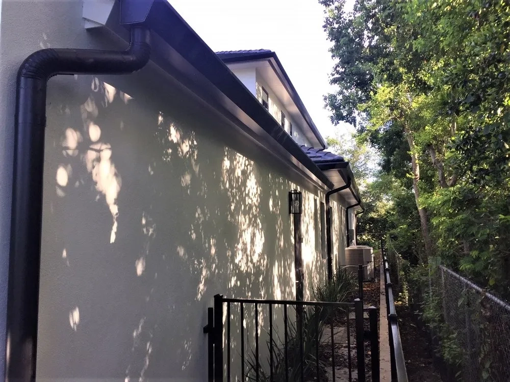 Black seamless gutter and downspout installation along residential side exterior