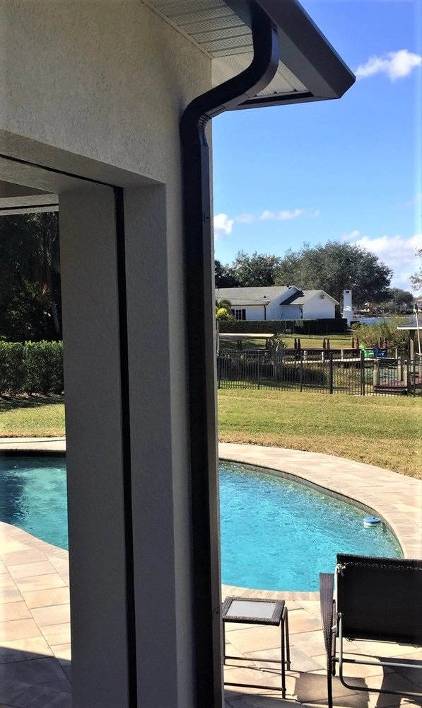 Black downspout installation beside covered patio and pool area