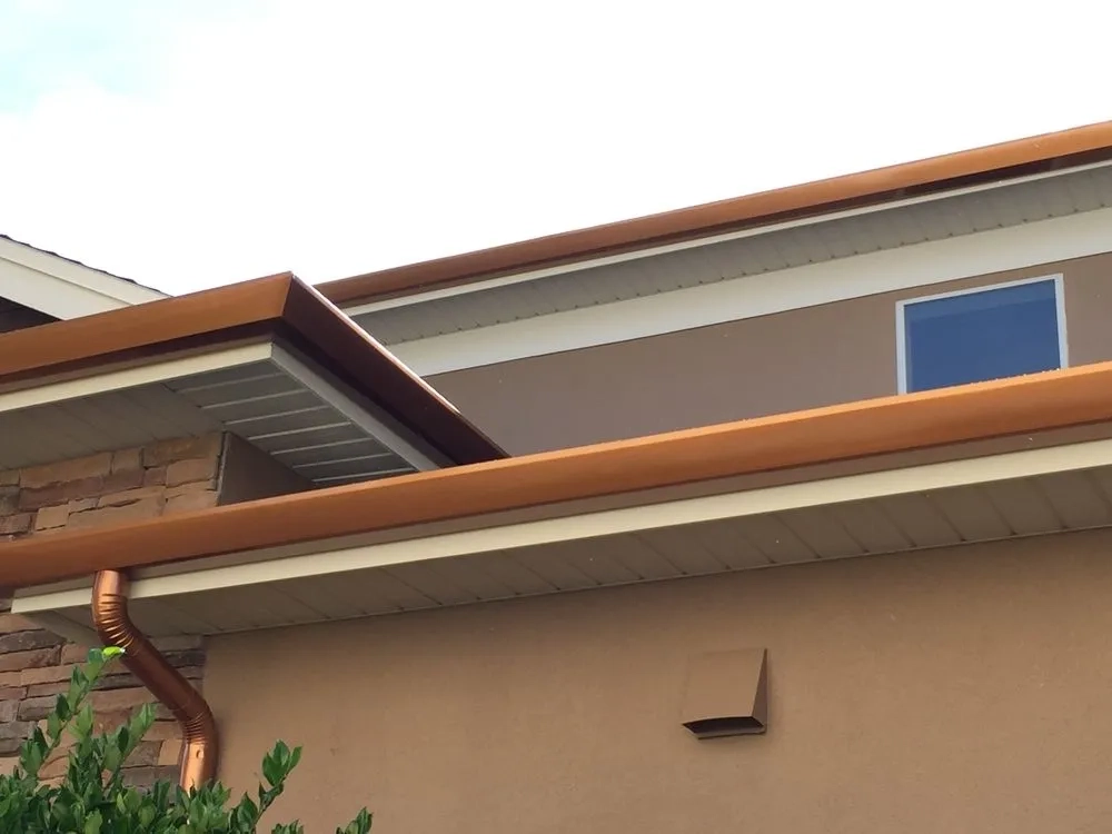 Copper-colored seamless gutter installation on modern residential home