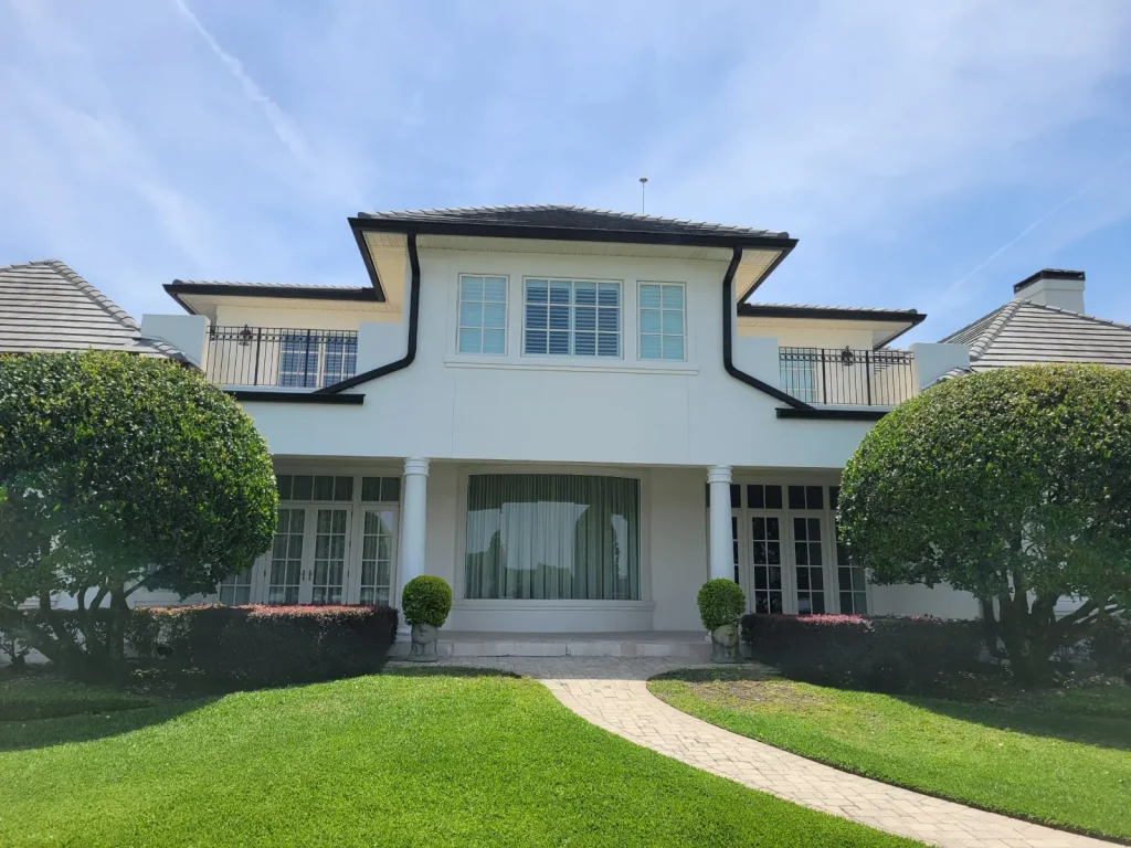 Precision Gutters FL seamless black gutter system installed on a luxury two-story white home, featuring clean roofline drainage, decorative architecture, and professionally fitted gutters for effective rainwater management.